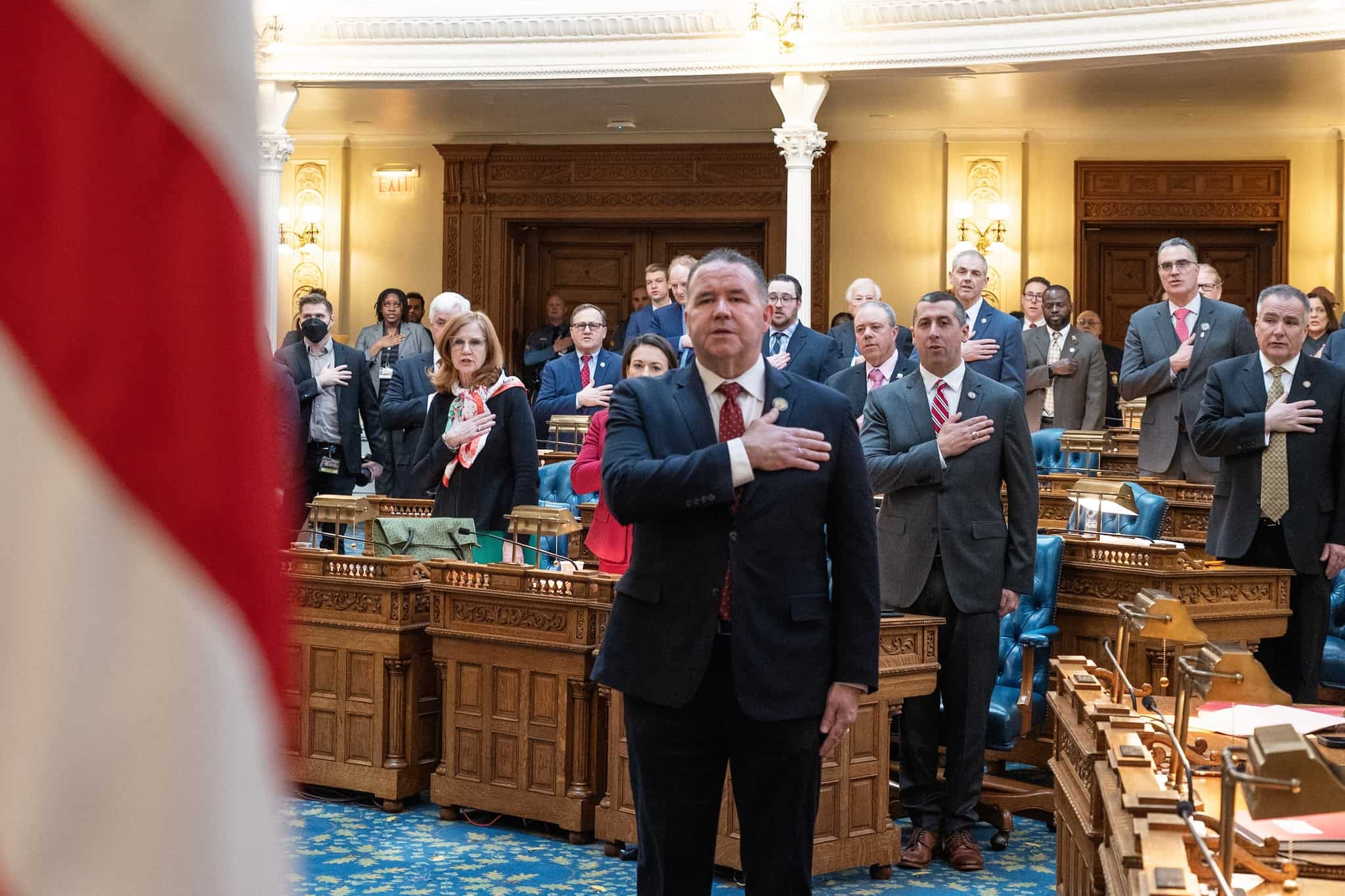 Alex Sauickie leading the New Jersey General Assembly in the flag salute, with a U.S. flag in the foreground.