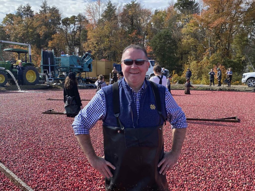 Assemblyman Alex Sauickie standing in a cranberry bog infant of a tractor and other people.